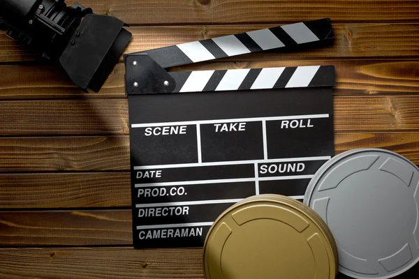 Tablero de aplausos con luz de película y carretes de película en la mesa de madera — Foto de Stock