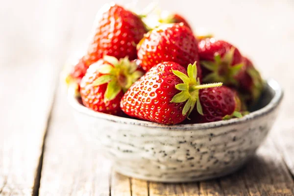 在木制桌子上的碗里放满成熟的红草莓 — 图库照片