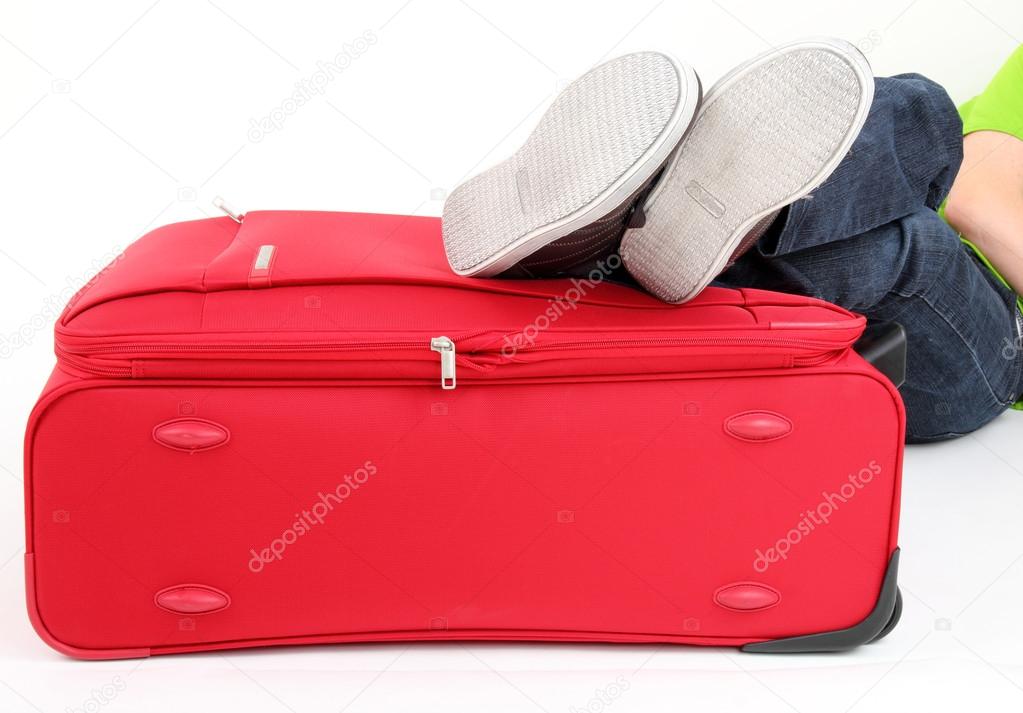 Young man lies on the red suitcase