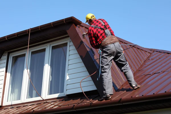 Roofer builder worker with pulverizer spraying paint on metal sheet roof — Stock Photo, Image