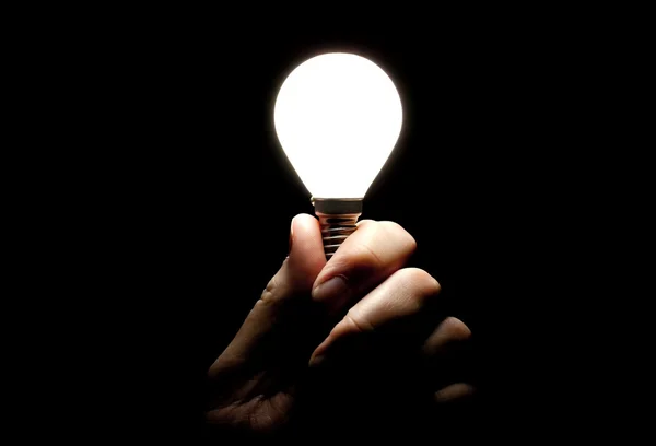 Glühbirne in der Hand gehalten auf schwarzem Hintergrund — Stockfoto