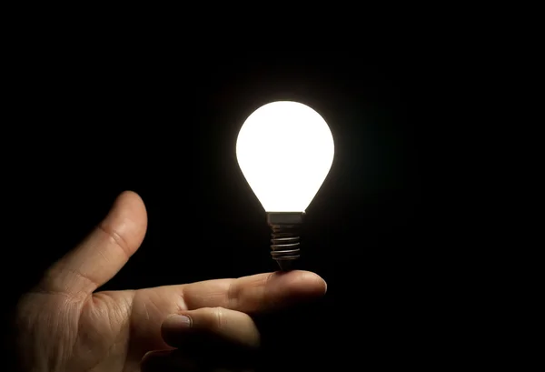 Lit light bulb balancing on finger — Stock Photo, Image