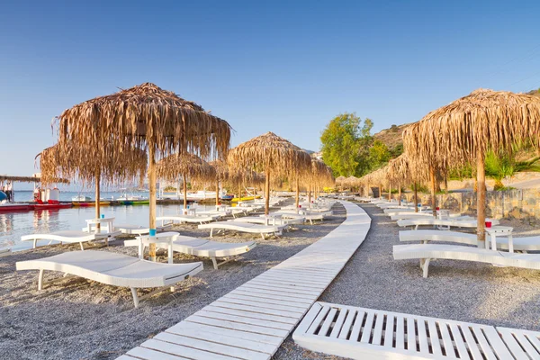 Camas de sol sob guarda-sol na praia pública de Creta — Fotografia de Stock