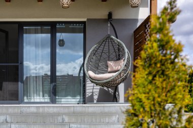 Modern hanging rattan chair with gray pillows on the summer garden terrace clipart