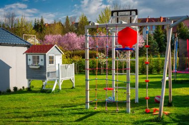 Green garden with a beautiful wooden house for children and a playground at blooming spring.