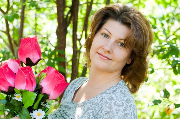 Woman with a bouquet of artificial flowers in summer park — Stock Photo, Image