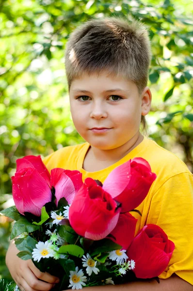 Um menino com um buquê de flores artificiais no parque de verão — Fotografia de Stock