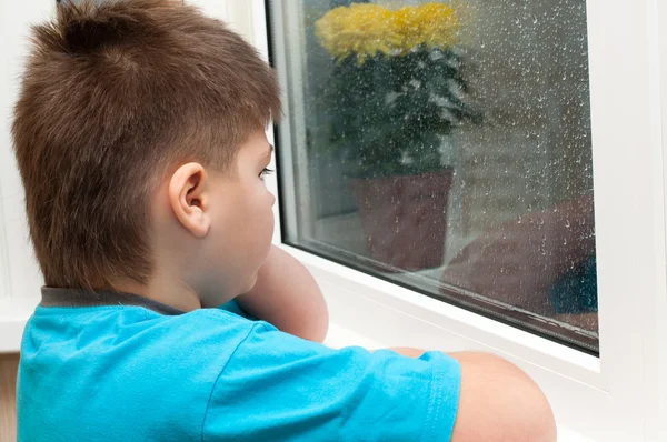 A boy looks out the window — Stock Photo, Image