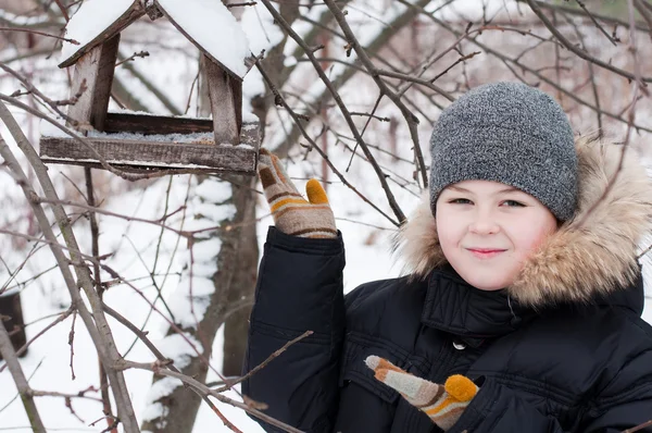 Pojken matar fåglarna i mataren i vinter — Stockfoto