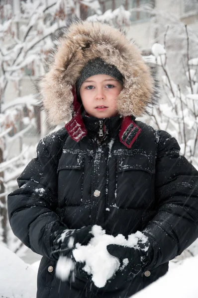 Retrato de um menino em roupas de inverno durante a queda de neve — Fotografia de Stock