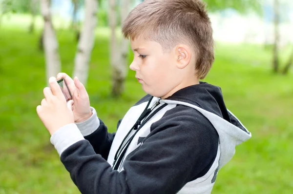 A boy plays on a mobile phone in a park — Stock Photo, Image