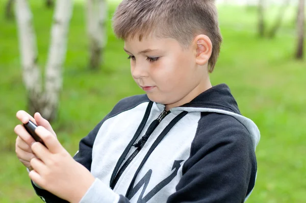 Een jongen speelt op een mobiele telefoon in een park — Stockfoto