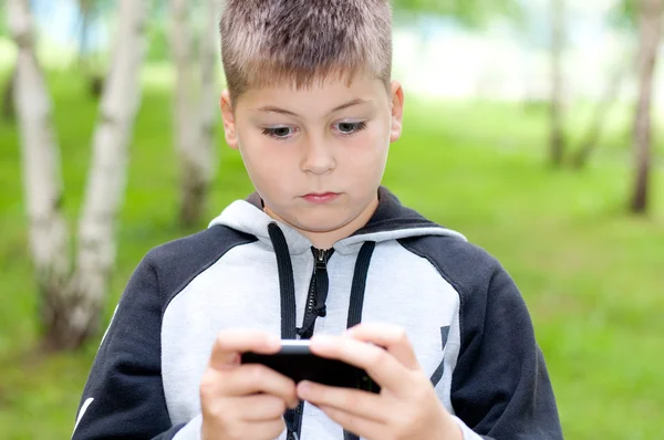 En pojke spelar på en mobiltelefon i en park — Stockfoto