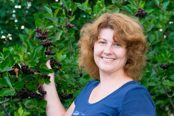 Een vrouw in een zwarte chokeberry bush in de tuin — Stockfoto