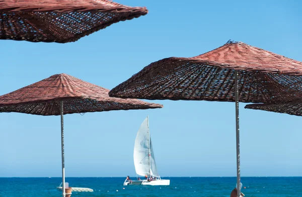 Sun umbrellas and sailboat at sea — Stock Photo, Image