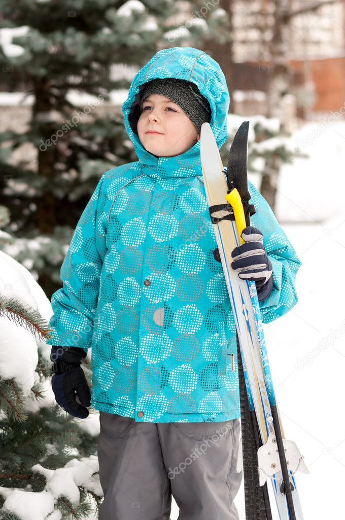 Boy with skis around snowy spruce