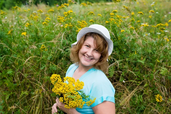 Middle-aged woman on a meadow with tansy — Stock Photo, Image