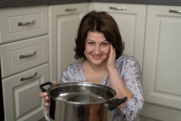 キッチンの背景に空の鍋を持っている笑顔の女性の肖像画 — ストック写真