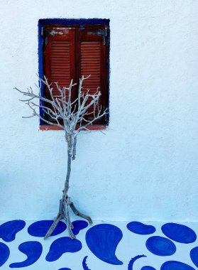 Duvarda beyaz alçı var. Penceredeki tahta panjurlar. Kuru odun. Yerde mavi desenler var..