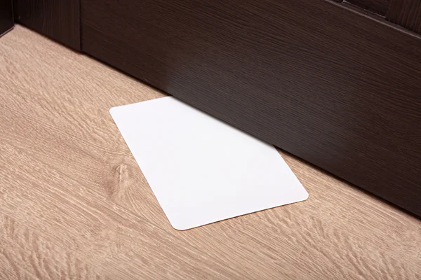 White envelope with message slipped under wooden door. Blank paper to write a nested in the gap under the wooden door. — Stock Photo, Image