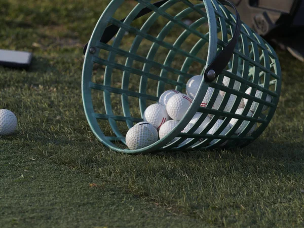 Golf ball on tee and golf balls in basket on green grass for practice