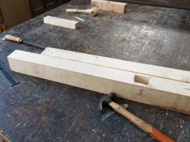 Marangozluk atölyesinde depolanan malzemeler ve arka planda aletler ve talaş ile meşe ağacı ahşap bar blokları.