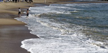 Günbatımında bir dalga'nın kenar yavaşça altlarında, köpük ile bir kumsalda yürüyen bir adamın çıplak ayak closeup Renk tonlu
