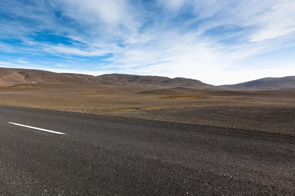 Highway through dry gravel lava field landscape under a blue sum — Stock Photo, Image