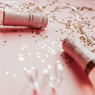 Noel ya da yeni yıl kompozisyonu. İçinde gül şampanyası şişeleri ve pastel pembe arka planda parlak parlak yıldız konfetileri var. Parti Yaratıcı Konsepti