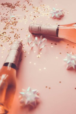 Noel ya da yeni yıl kompozisyonu. İçinde gül şampanyası şişeleri ve pastel pembe arka planda parlak parlak yıldız konfetileri var. Parti Yaratıcı Konsepti