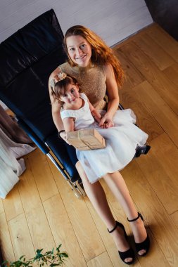 Beyaz elbiseli küçük bir kız ve sevgili annesi evde, saksının yanında oturuyor.