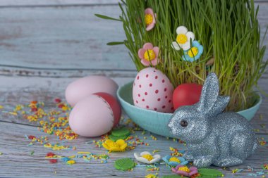 Paskalya kompozisyonu yumurta, tavşan, tatlı çiçekler ve çimenler, ahşap arka planda.