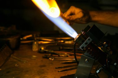 Cam üfleme imalatı. Ateş cam üfleyici ocakla bardağı boş ısıtır. El yapımı cam işçiliği