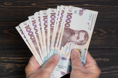 Ukrayna 'nın parası. Tahta masadaki eldivenli ellerde bulunan bir yığın Ukrayna Hryvnia banknotları. Hryvnia 1000 uah