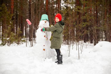 Girl in  green coat in winter in   forest near   snowman.