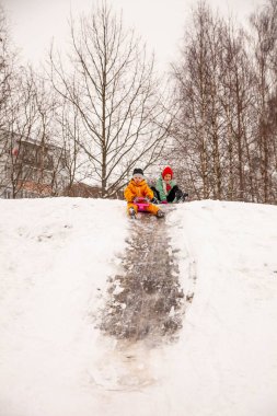 Happy children riding down   ice slide on   sled