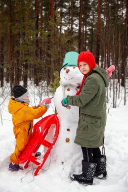 Children of nine and three years old   on   winter walk near   snowman 