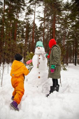 Children of nine and three years old   on   winter walk near   snowman 