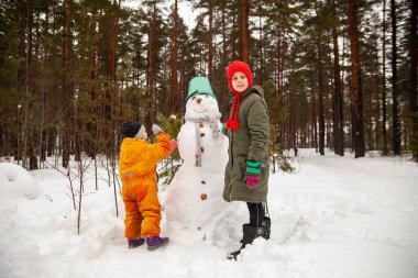 Children of nine and three years old   on   winter walk near   snowman 