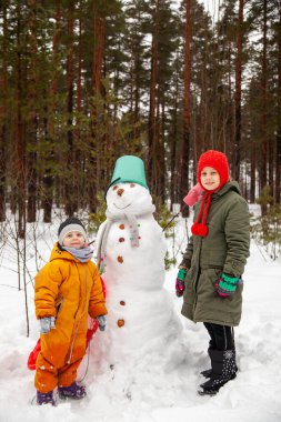 Children of nine and three years old   on   winter walk near   snowman 