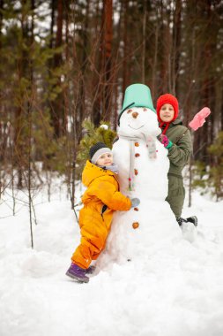 Children of nine and three years old   on   winter walk near   snowman 