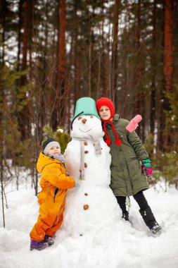 Children of nine and three years old   on   winter walk near   snowman 