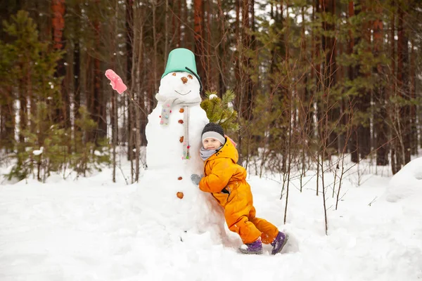 Girl in   yellow jumpsuit in winter in   forest near   snowman.