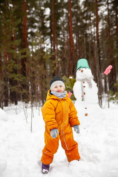 Girl in   yellow jumpsuit in winter in   forest near   snowman.