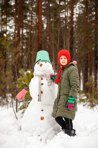 Girl in  green coat in winter in   forest near   snowman.