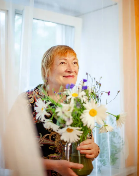 家の中で生きている野花の花束を持つ高齢女性 — ストック写真