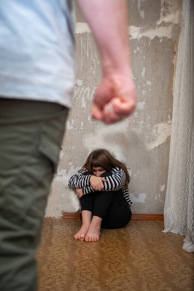 Портрет испуганной девочки-подростка, сидящей у стены напротив агрессивного мужчины с ремнем в руке. 