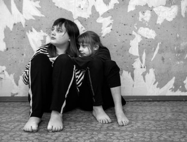 9 ve 12 yaşlarında iki çıplak ayaklı, korkmuş ve üzgün kız eski beton duvarda yan yana oturuyorlar.