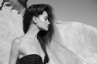 Güzel, zarif bir bayan sahilde siyah mayoyla poz veriyor. Denizde seksi esmer