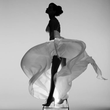 Beautiful young lady posing in a photo studio in a chic dress. Sexy model in bright spotlights. Portrait of a woman in a white wedding dress. Art photography.